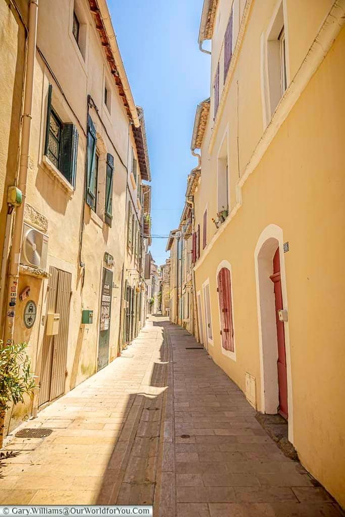 Sunlit narrow lane lined with traditional pastel houses and shuttered windows in the historic centre of Saint-Rémy-de-Provence.