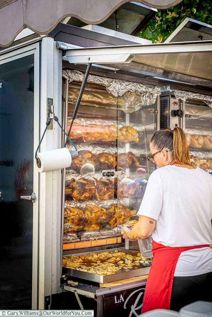 Rotisserie chickens roasting above golden potatoes at a traditional food stall in Saint-Rémy-de-Provence market, southern France.