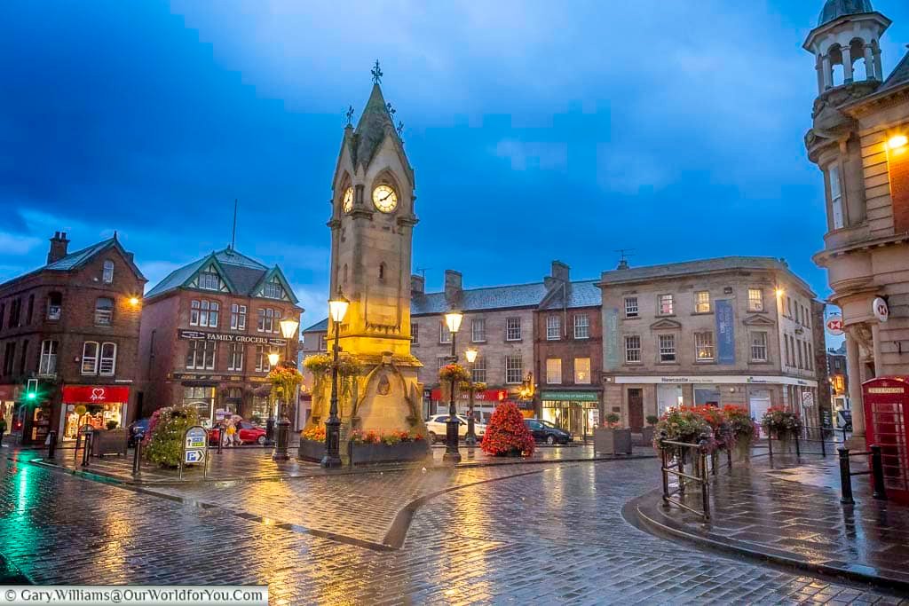 Penrith’s historic Market Square glows beneath evening streetlights, with the illuminated Musgrave Monument reflected on rain-soaked cobblestones. The atmospheric scene captures the character and charm of this traditional Cumbrian market town after dark.