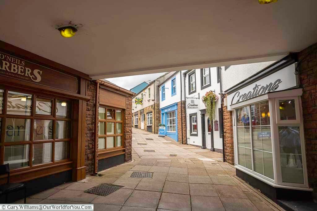 A quiet pedestrian passageway in Penrith leads past traditional shopfronts and historic buildings, decorated with hanging flower baskets. This picturesque walkway is one of the charming little corners to discover while exploring Penrith town centre.